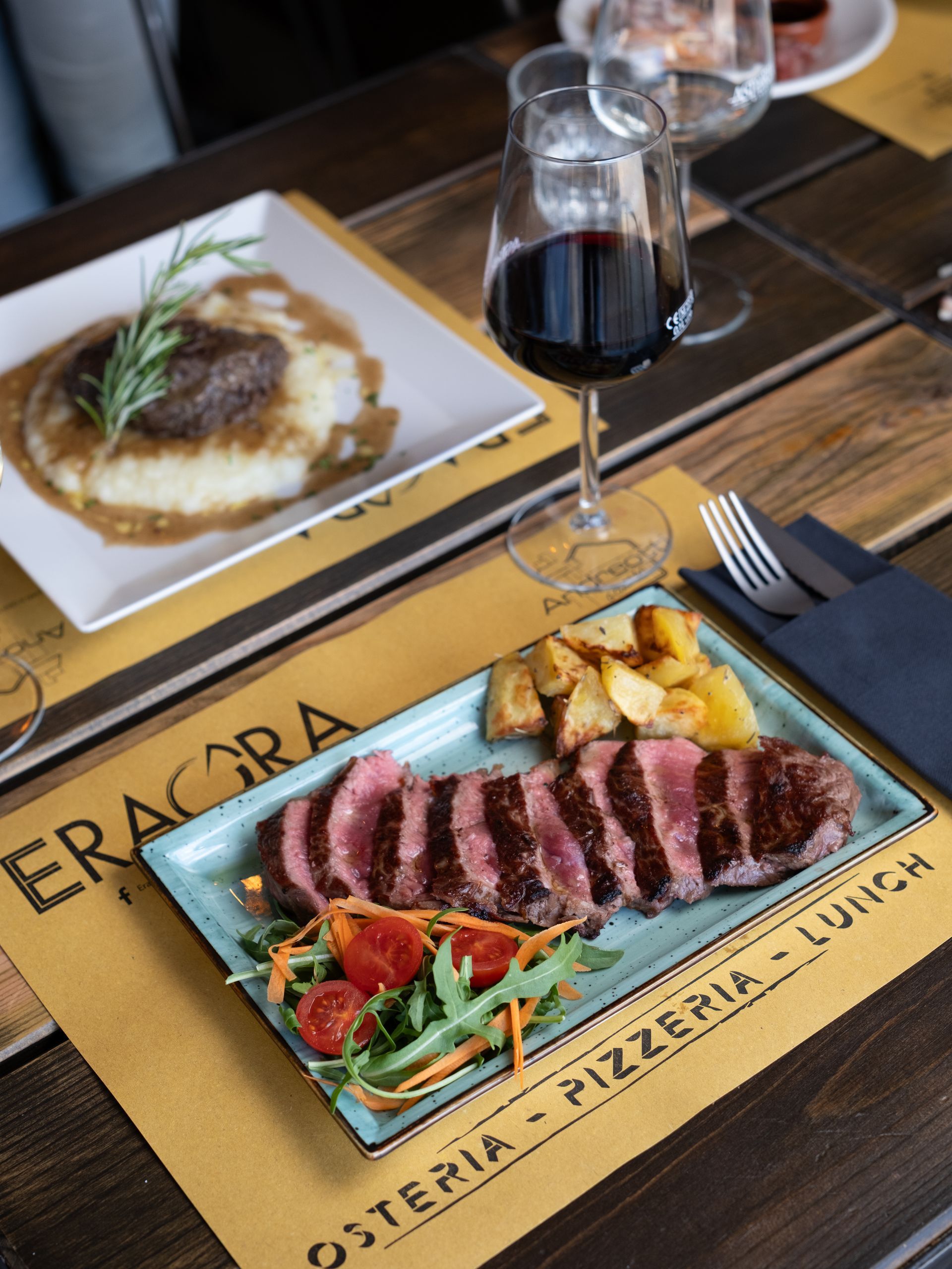 Bistecca tagliata con patate arrosto, insalata e un bicchiere di vino rosso sul tavolo di un ristorante.