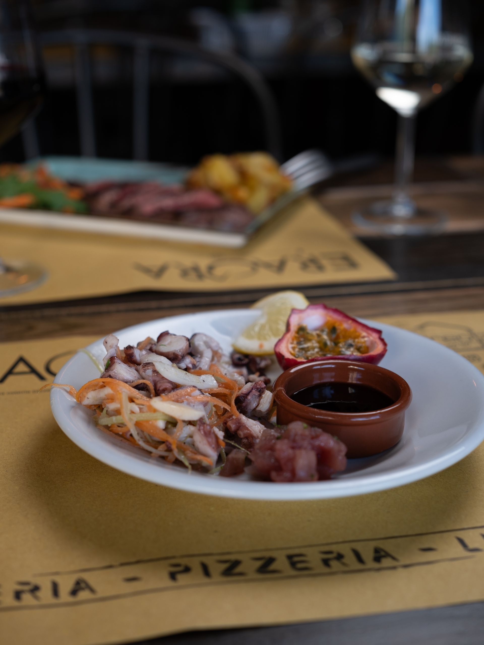 Piatto di frutti di mare, tra cui polpo, con frutto della passione e salsa, su un tavolo di un ristorante.