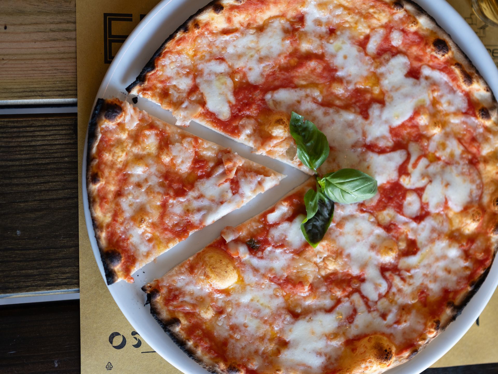 Pizza Margherita su un piatto bianco, con una fetta tagliata e guarnita con foglie di basilico.