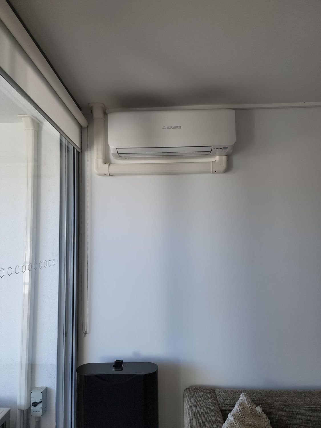White air conditioner on a white wall, near a window and black speaker in Nowra