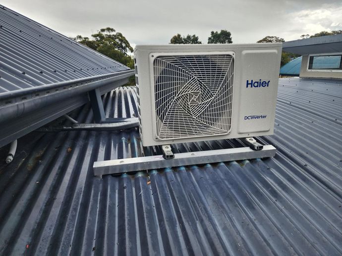 Two Denali Air Conditioning workers in work shirts installing an air conditioner unit next to a building in Nowra