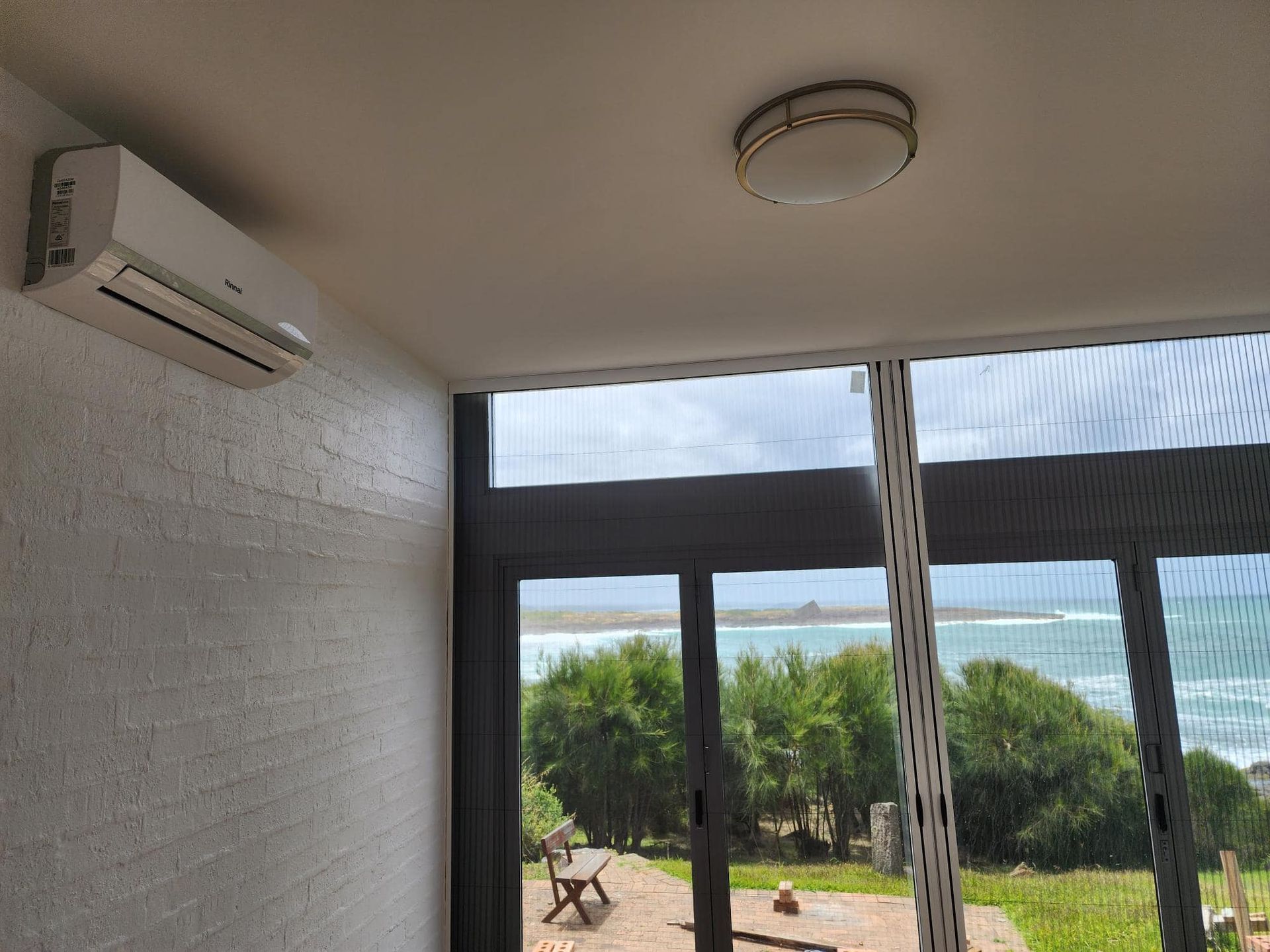 Air conditioner on textured wall, window overlooking ocean and vegetation in Nowra
