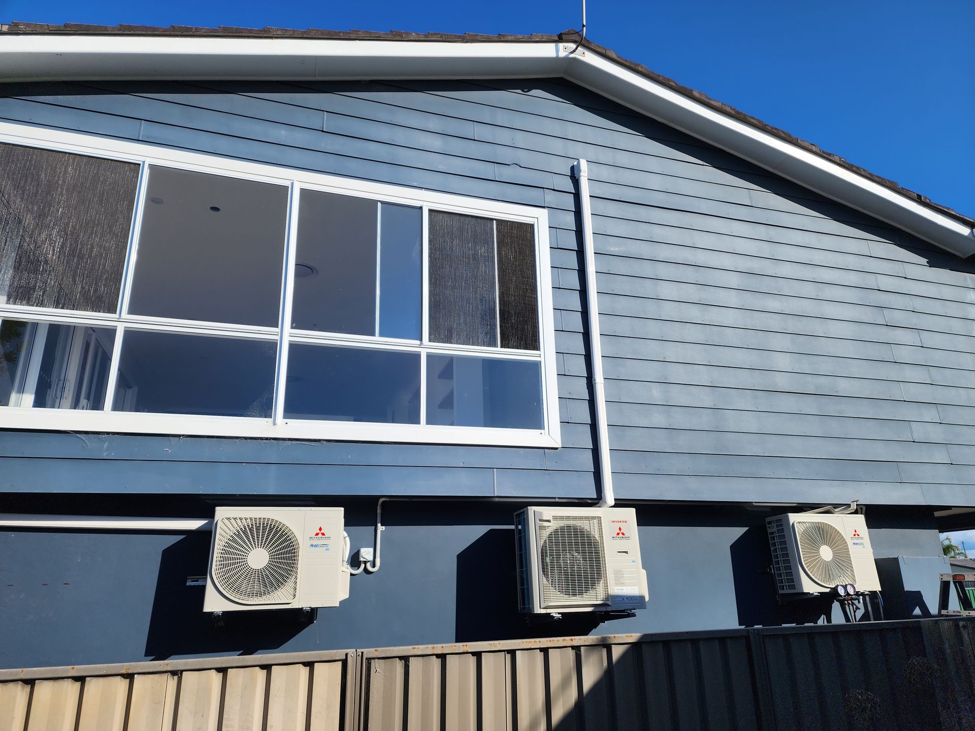 Blue house exterior with large window, three air conditioning units, and a wooden fence.