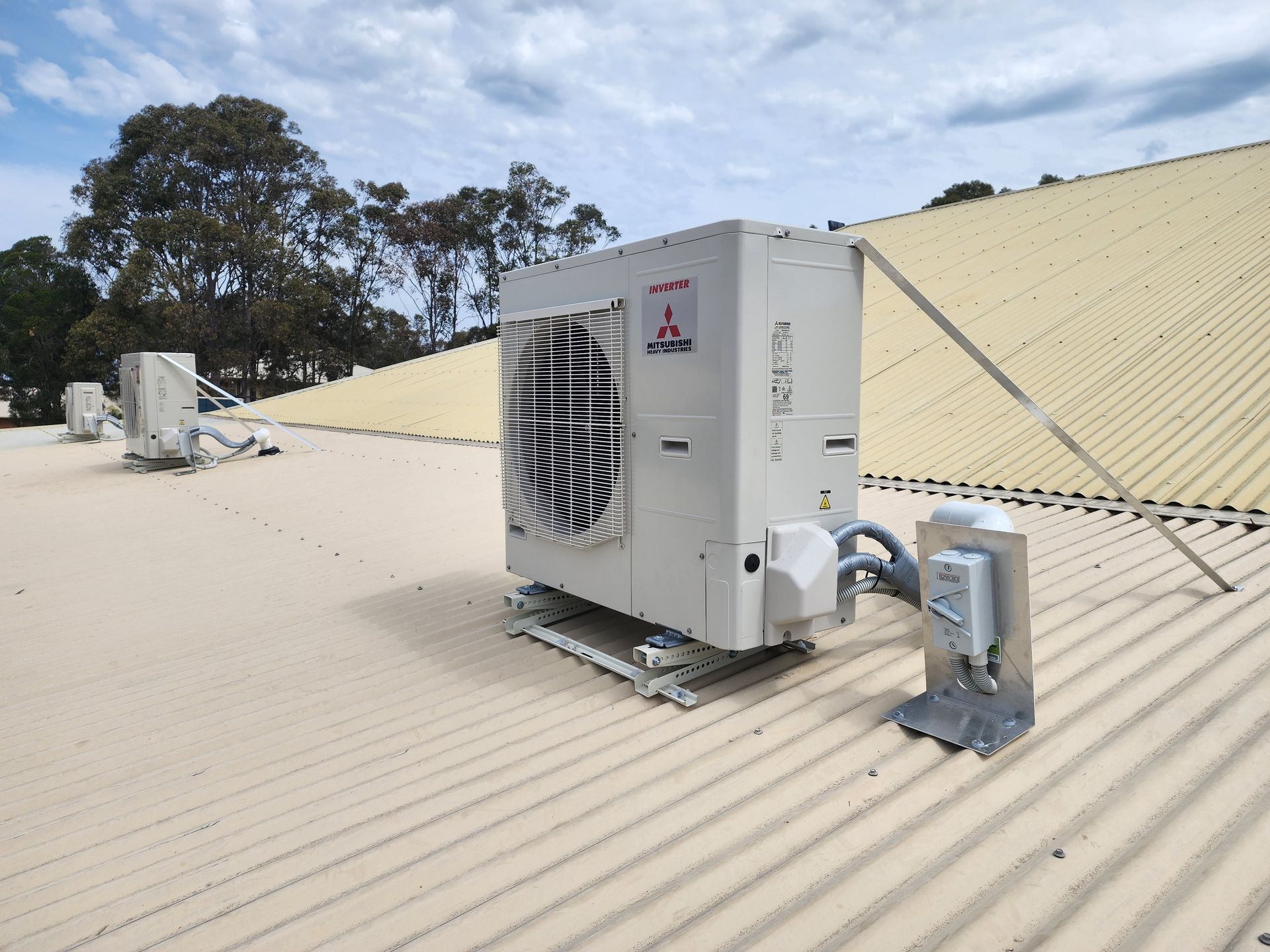 Air conditioning unit on a corrugated roof with support brackets under a cloudy sky.