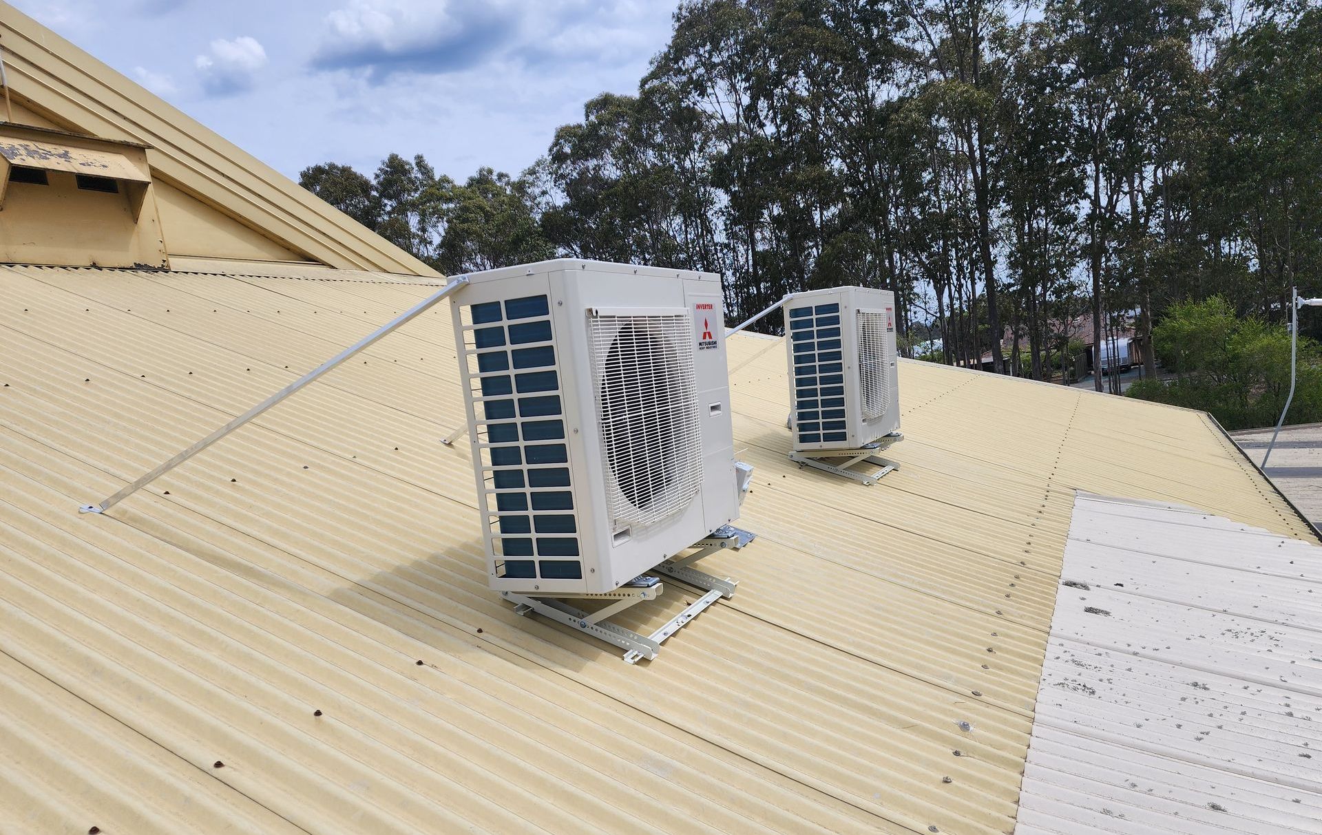 Two Denali Air Conditioning workers in work shirts installing an air conditioner unit next to a building in Nowra