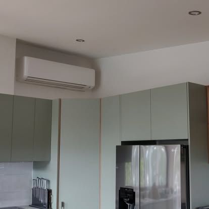 Air conditioner above light green kitchen cabinets and stainless steel refrigerator.