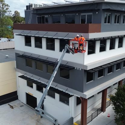 Two Denali Air Conditioning Nowra workers in orange vests on lift platform, working on a modern building exterior.