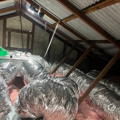 Attic with silver insulated HVAC ductwork, wooden beams, and insulation.
