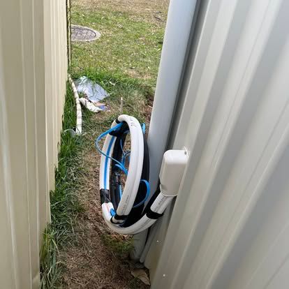 A rolled-up white and blue hose hangs next to a white corrugated metal wall and fence in a yard in Nowra