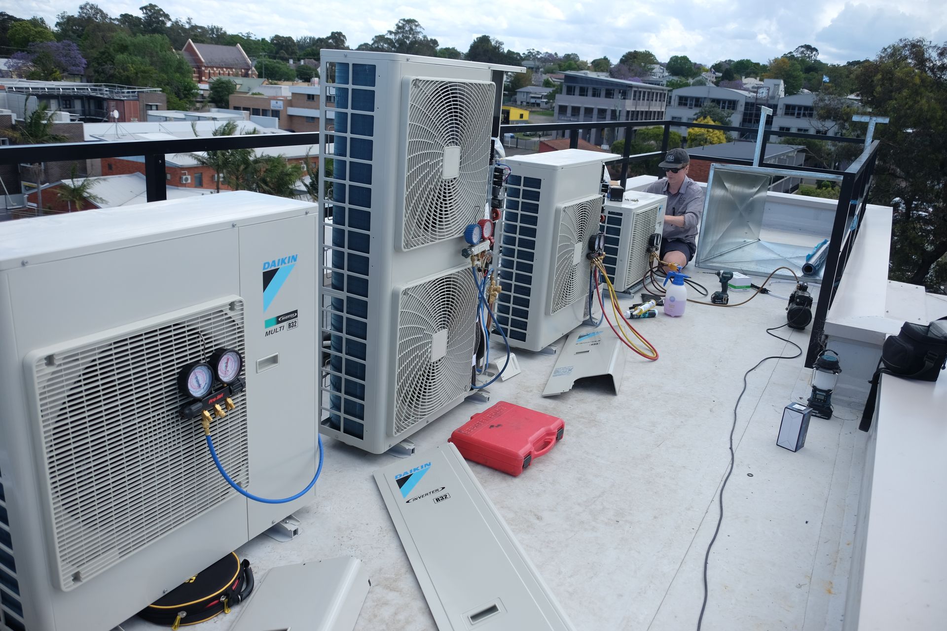 Two Denali Air Conditioning workers in work shirts installing an air conditioner unit next to a building in Nowra