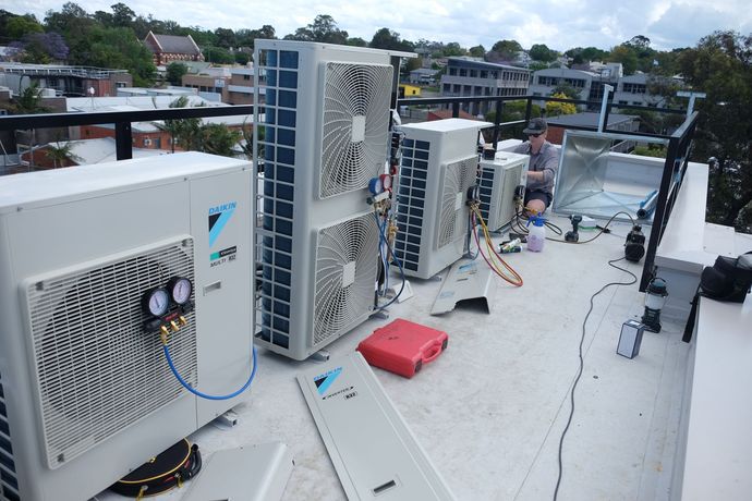 Two Denali Air Conditioning workers in work shirts installing an air conditioner unit next to a building in Nowra