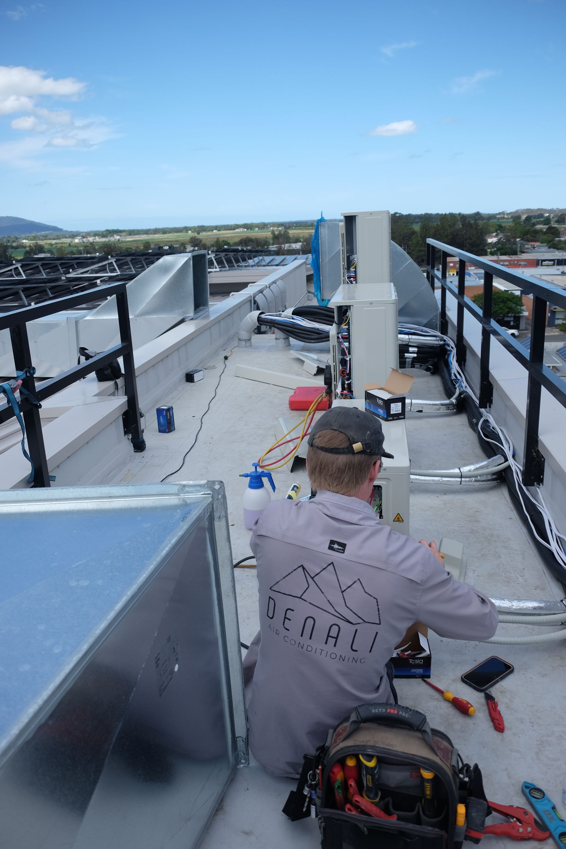 Denali Air Conditioningon a rooftop, working on HVAC system, sunny day with cityscape view.