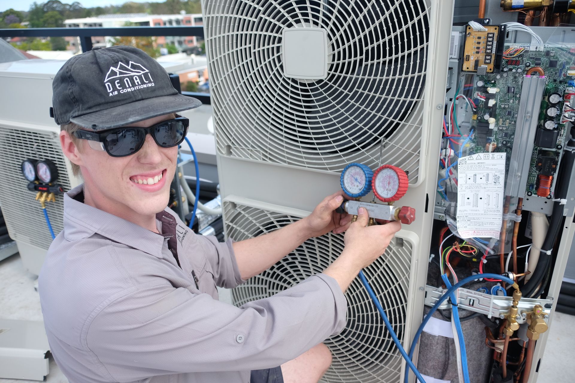 Denali Air Conditioning technician wearing sunglasses, working on an AC unit outdoors in Nowra