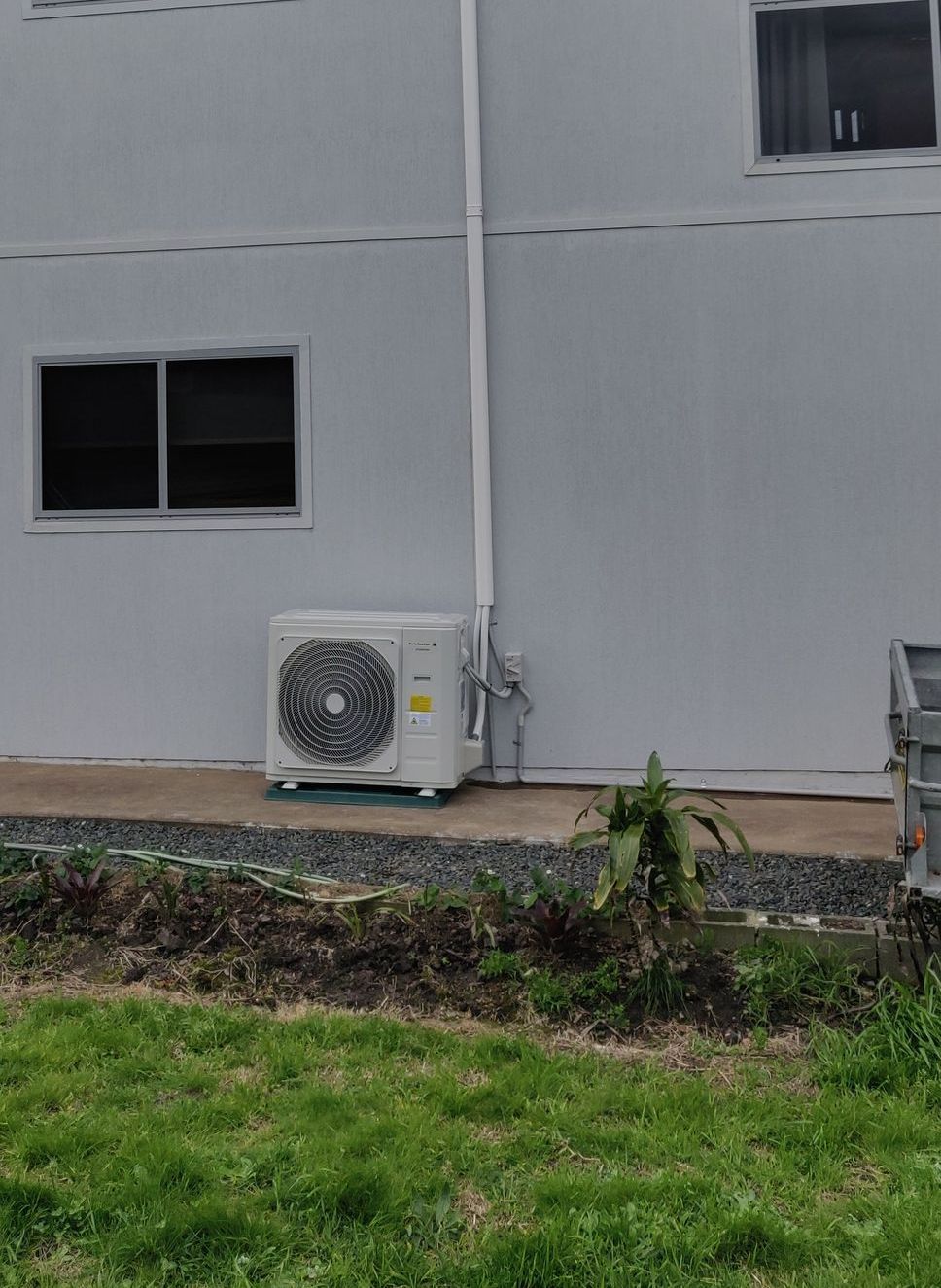Air conditioner unit mounted on a light gray building with a window in Nowra