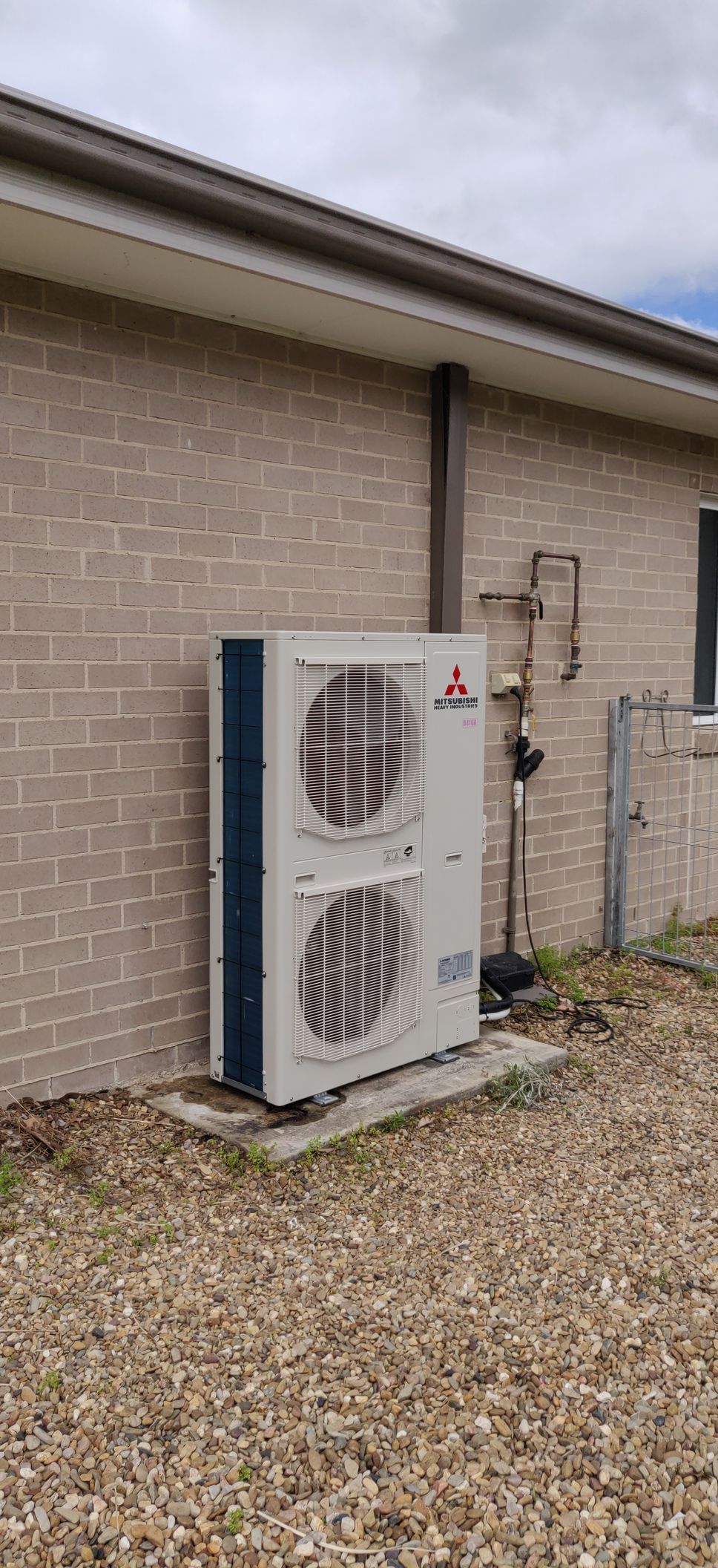 A Mitsubishi Air Conditioning unit against a brick wall on a bed of gravel.