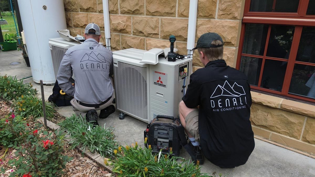 Two men are working on an air conditioner outside of a building.