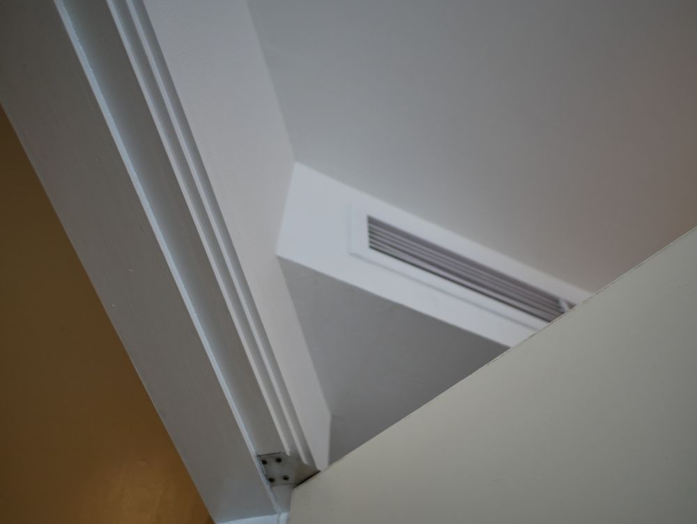 Two Denali Air Conditioning workers in work shirts installing an air conditioner unit next to a building in Nowra