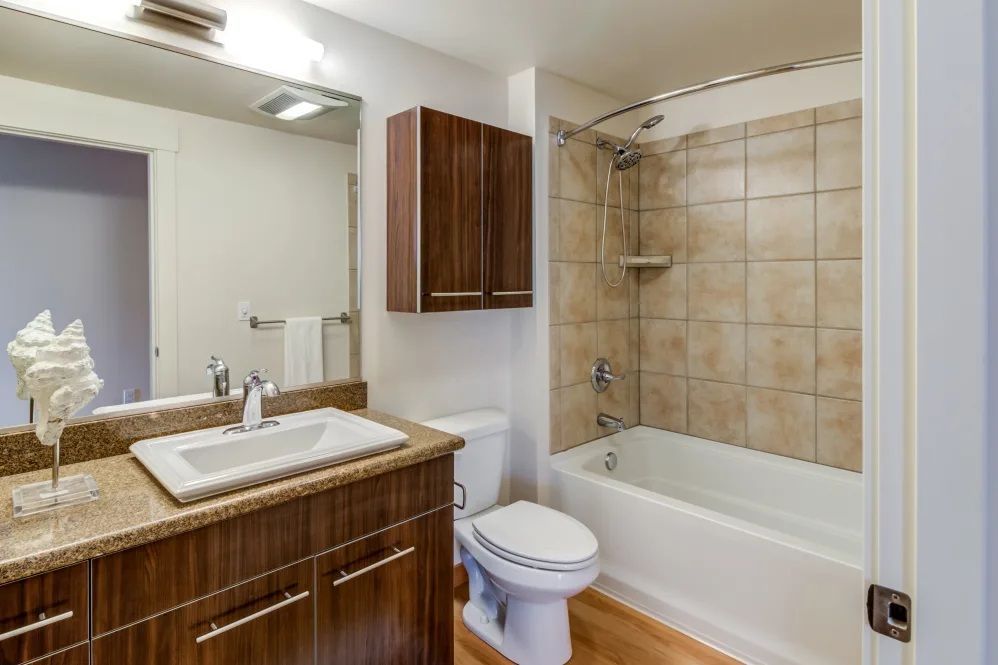 Bathroom with vanity, toilet, and bathtub. Brown cabinets, tan tiled shower, and wood floor.