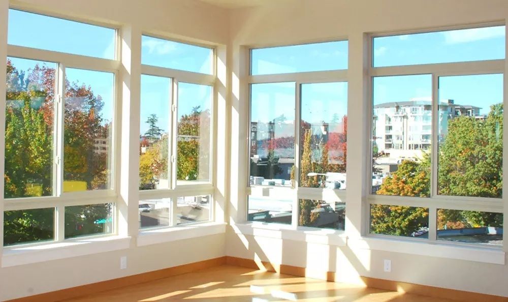 Bright room with large windows overlooking trees and buildings, sunny day.
