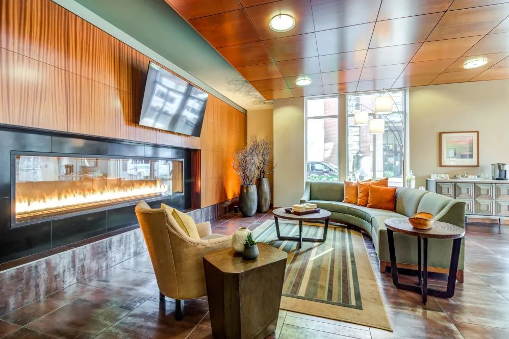 Lounge with fireplace, curved sofa, and wood paneling. Brown, green, and orange color scheme.
