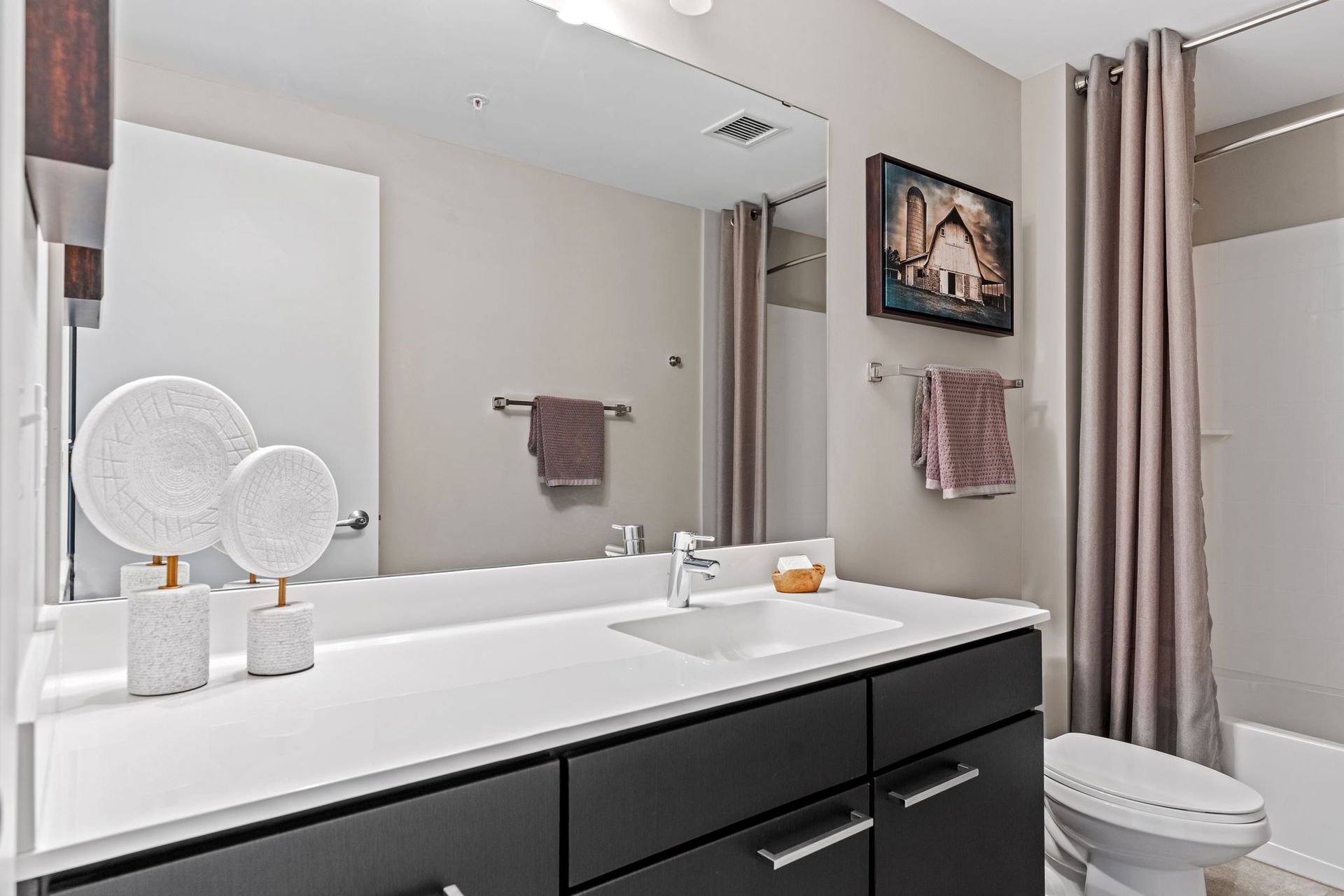Modern bathroom with gray walls, dark vanity, large mirror, and tan shower curtain.