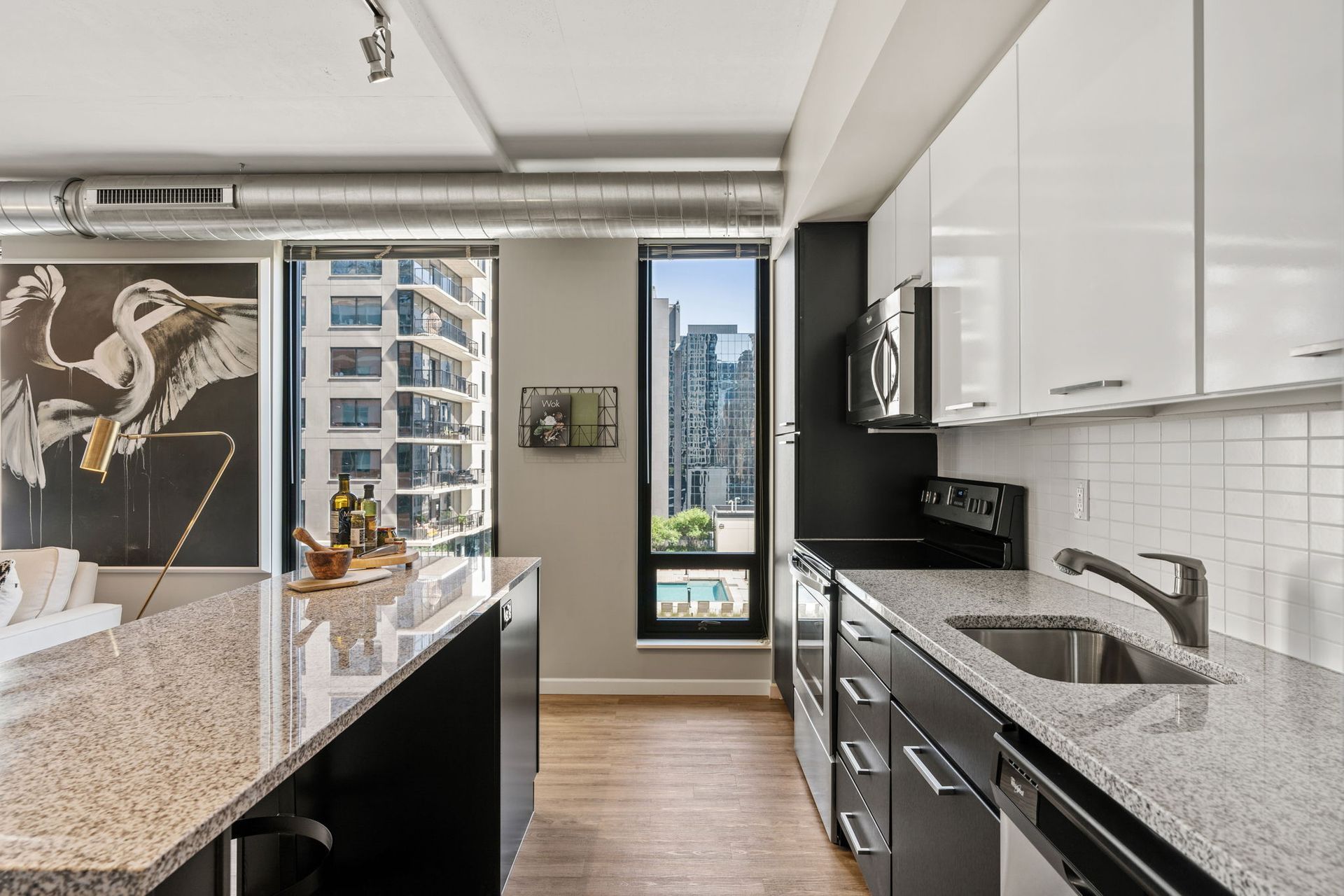 Modern kitchen with white and black cabinets, island with granite countertop, city view.