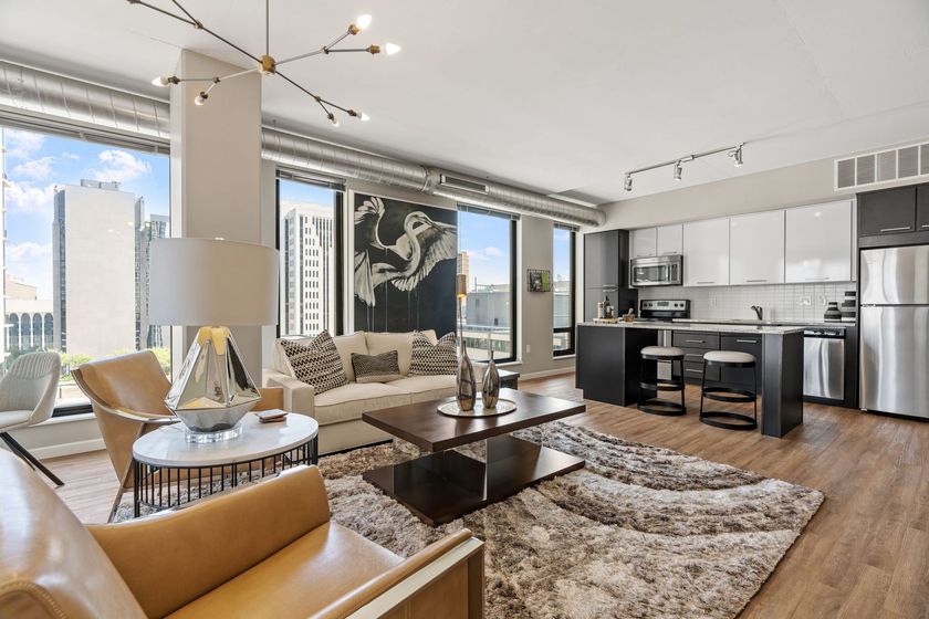 A living room with a couch , chairs , a coffee table and a kitchen.