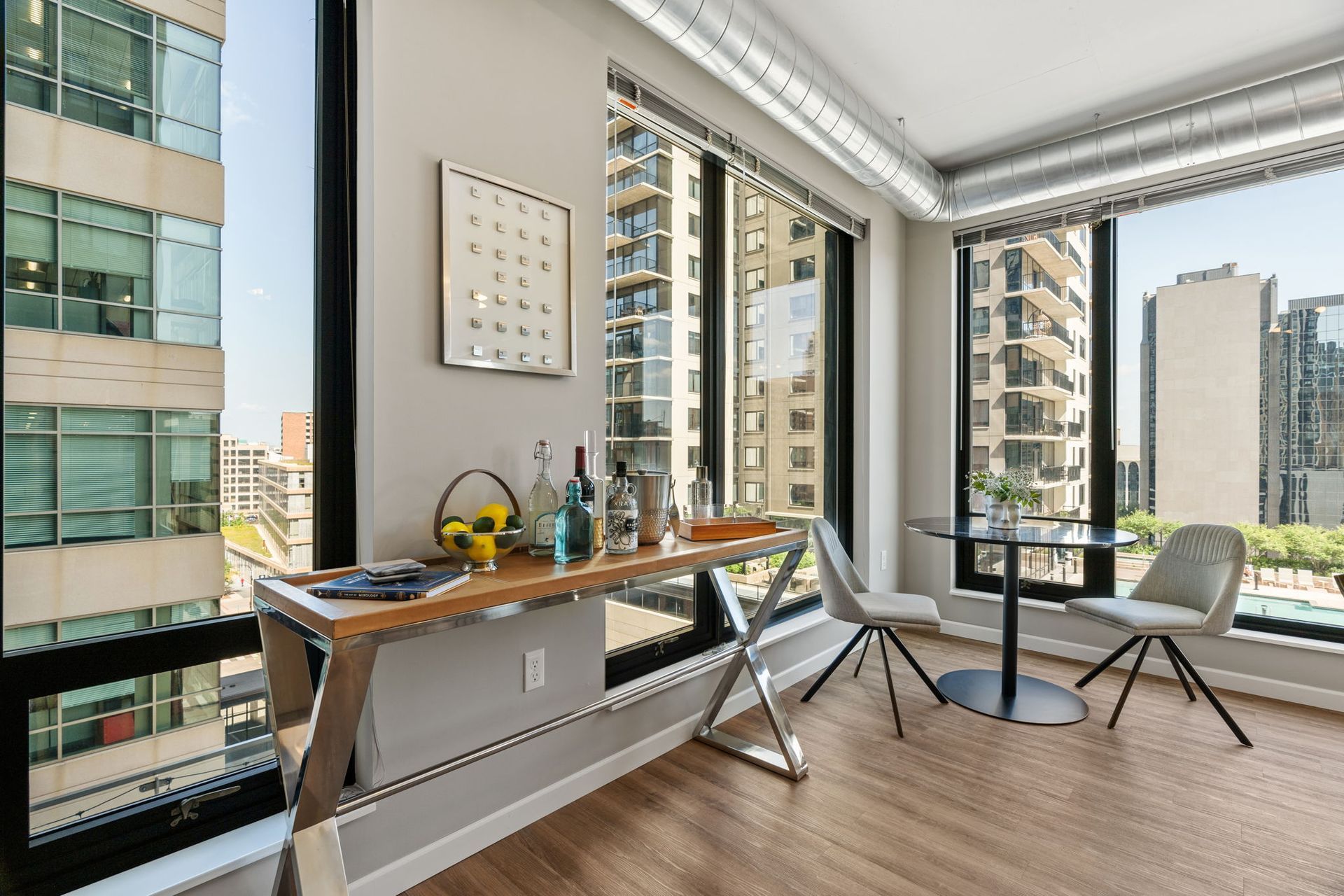 Living area with bar, small table, city views. Wooden floor, metal accents, neutral colors.