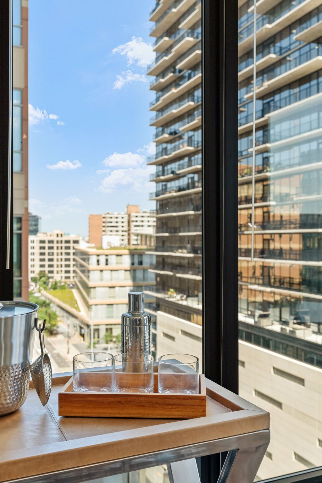Cocktail tray with shaker and glasses by a large window with a city view.
