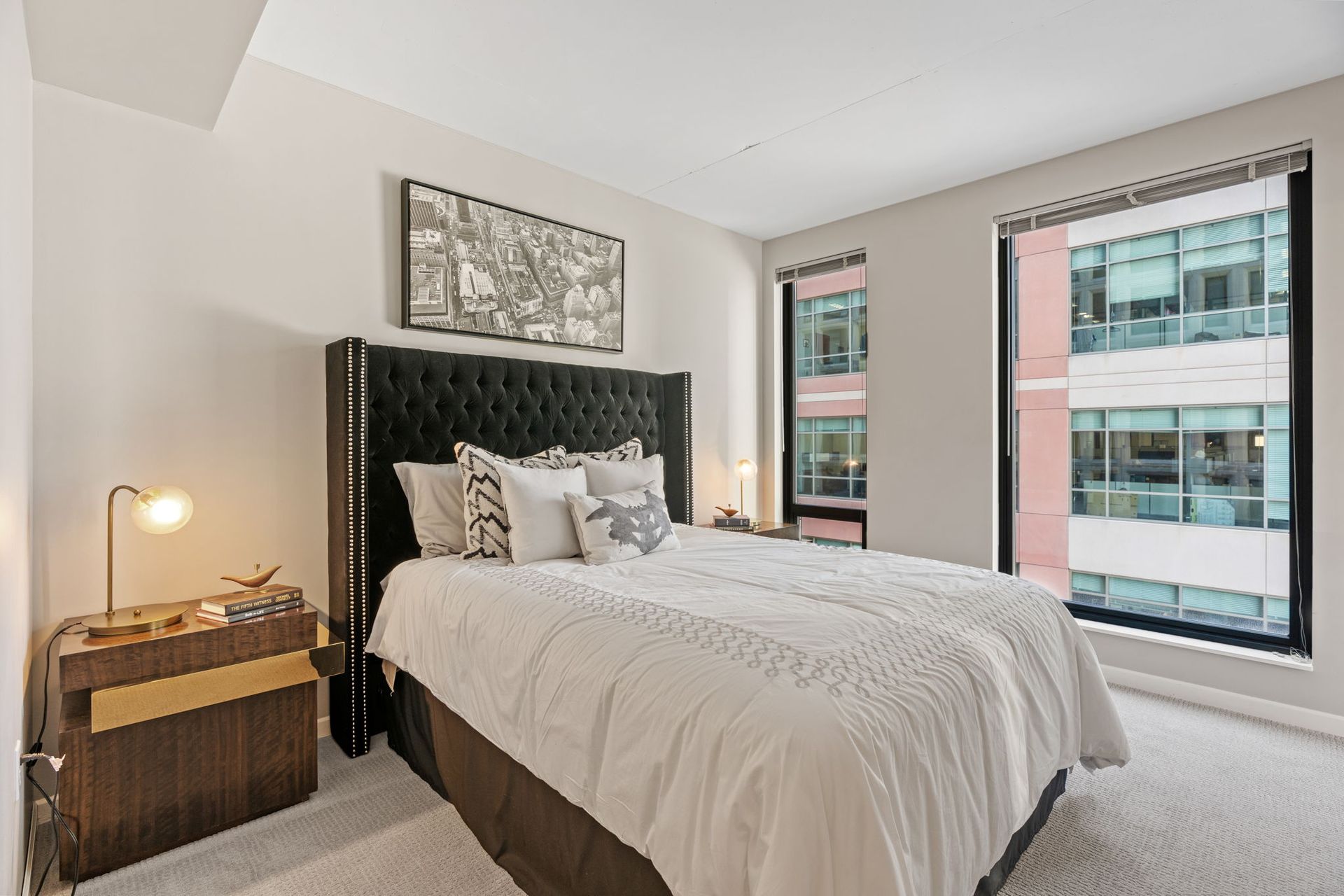 A bedroom with a bed , two windows and a painting on the wall.