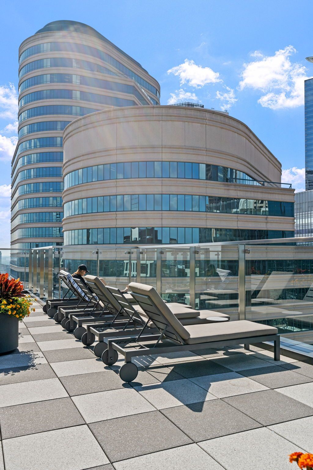 Rooftop with lounge chairs, two curved buildings in the background, sunny day.