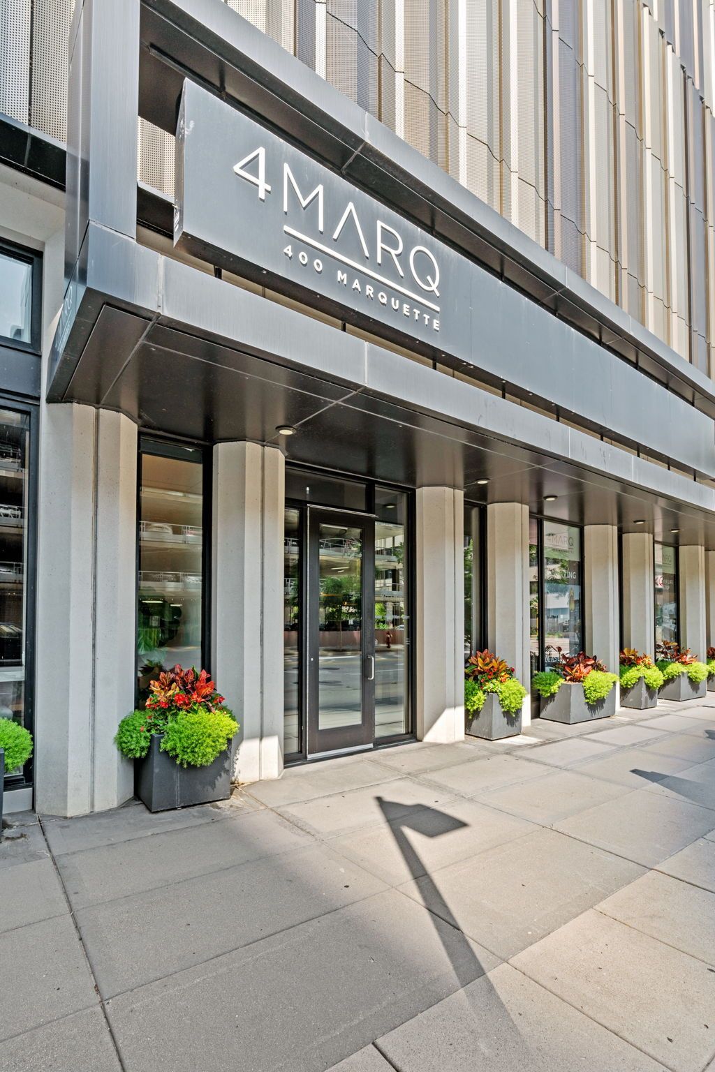 Entrance to 4 Marq building with a black awning, gray columns, and potted plants.