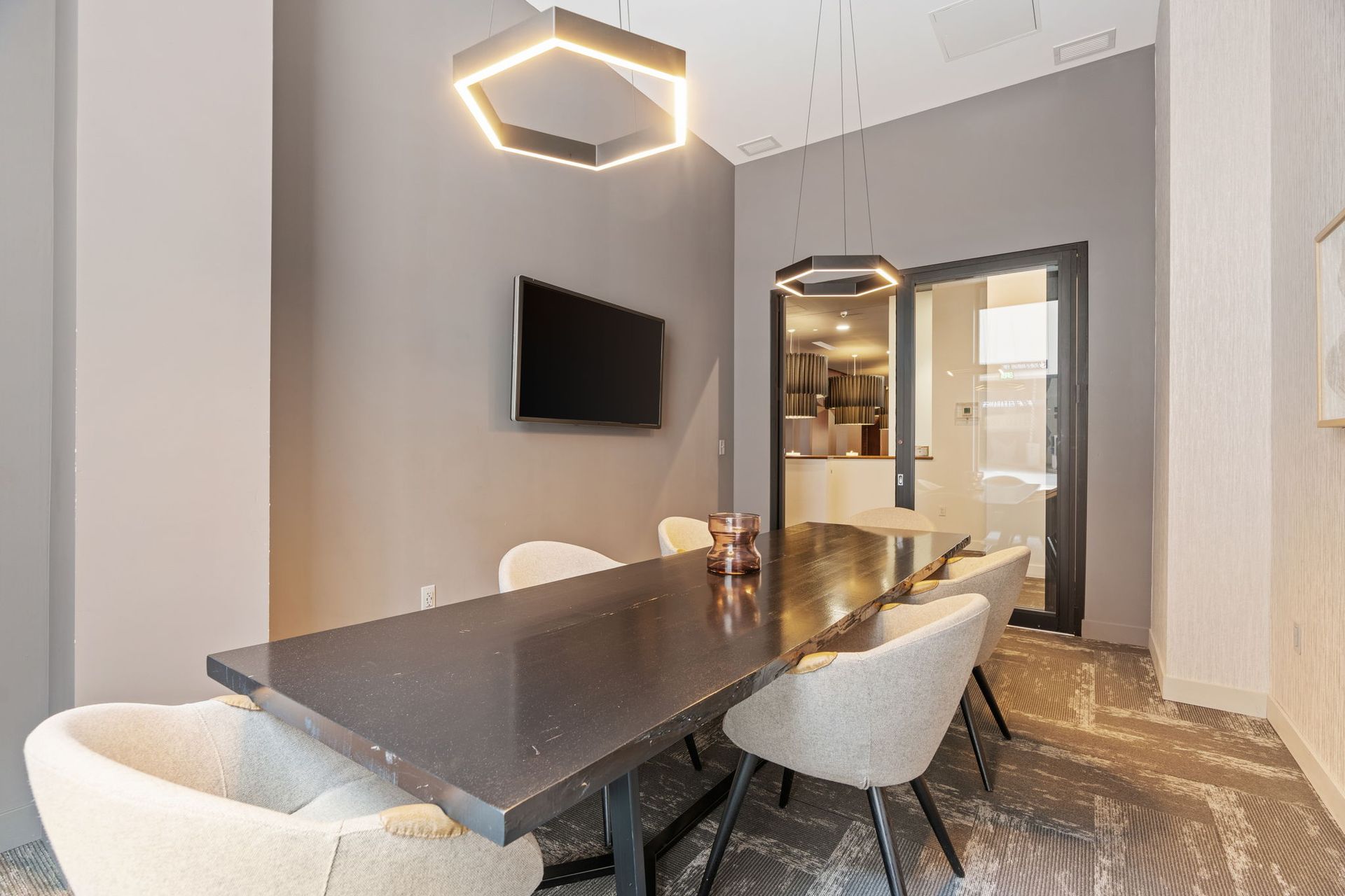 Modern meeting room with table, chairs, TV, and geometric lights.