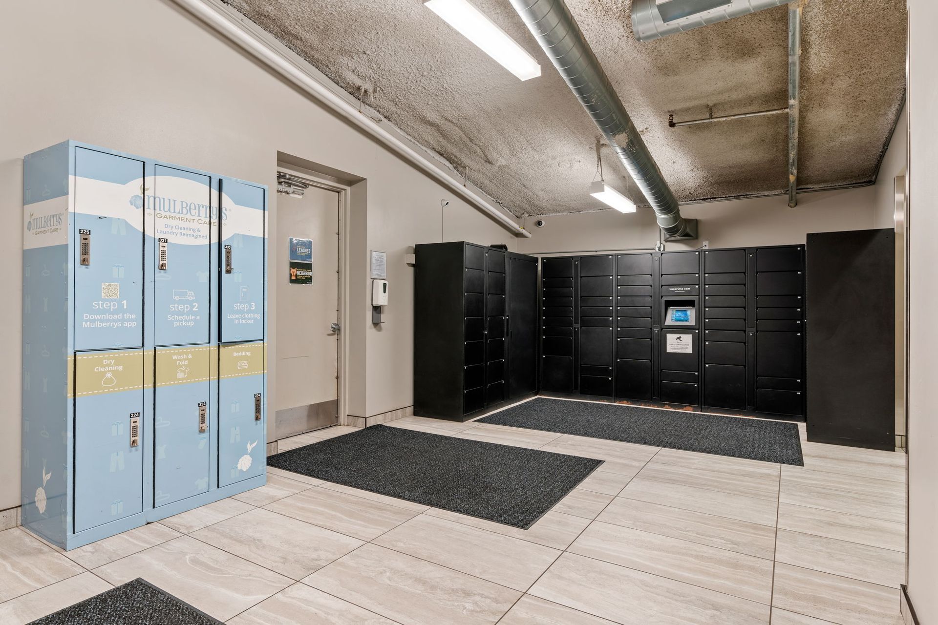 Lockers in a room with gray and blue lockers, door, tiled floor, and two black mats.