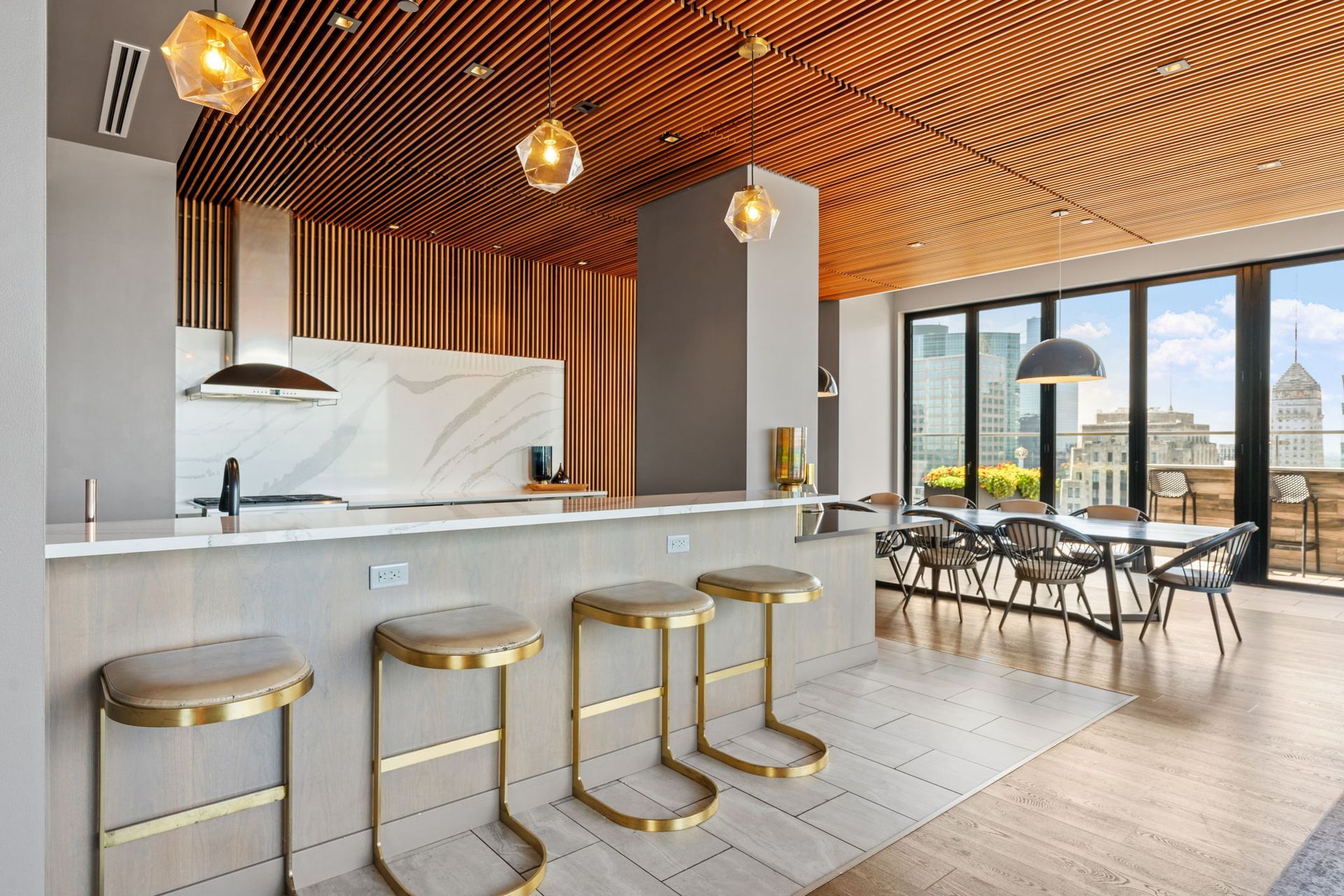 Modern kitchen with gold accents, wooden ceiling, bar stools, and city views.