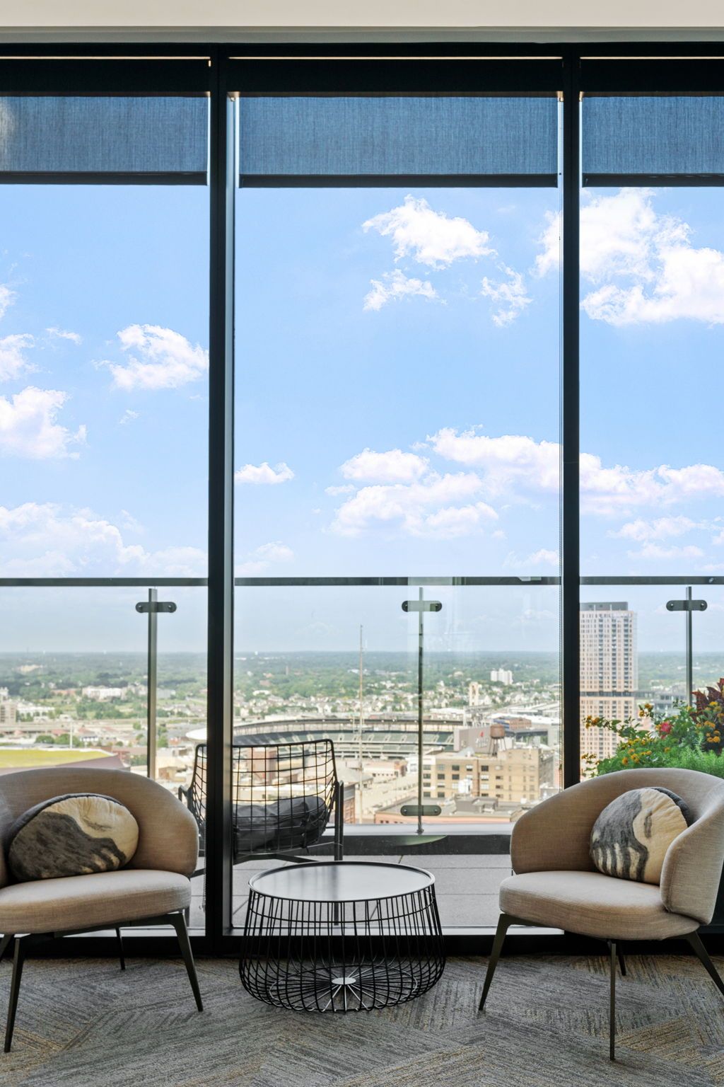 Two chairs and a table by a window with city views. Blue sky and clouds are visible.