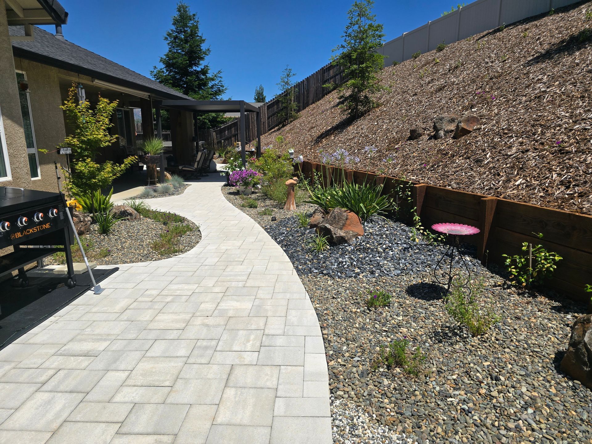 A brick walkway leading to a house with a fence in the background.