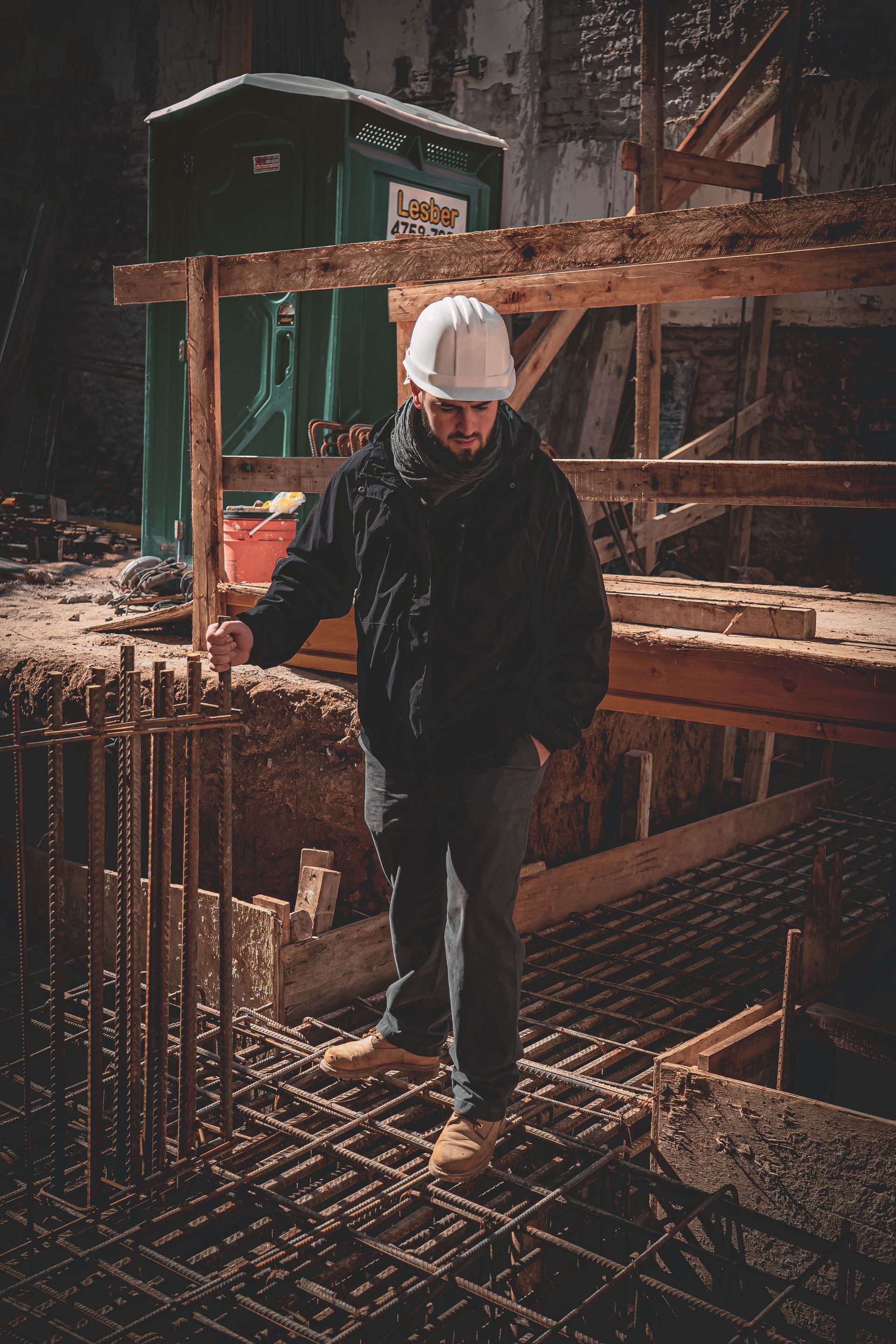 Worker in a hard hat standing on a rebar grid at a construction site, with wooden forms in the background.