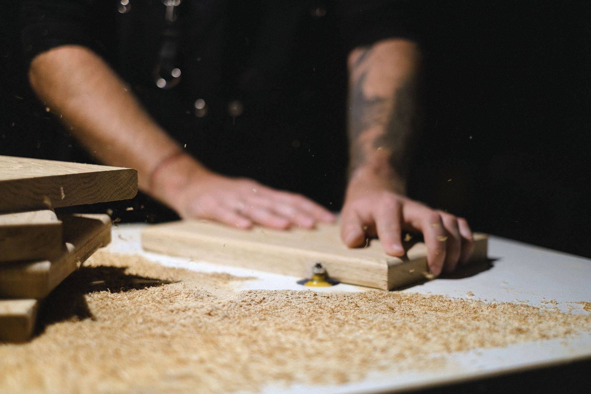 Hands measuring wood on a workbench with sawdust and stacked lumber