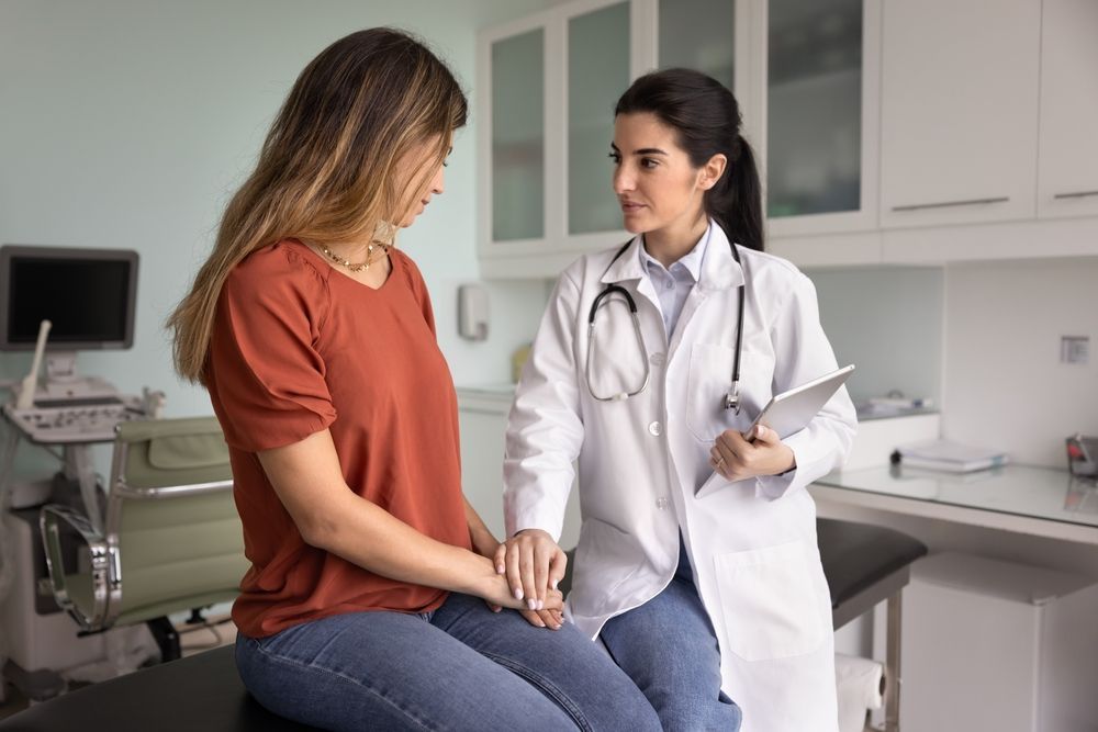 Doctor comforting patient in a medical office; doctor holding tablet, patient looking down.