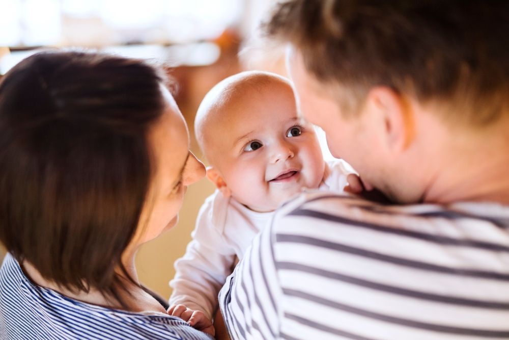 Smiling baby held by parents; indoor setting, looking at the camera.