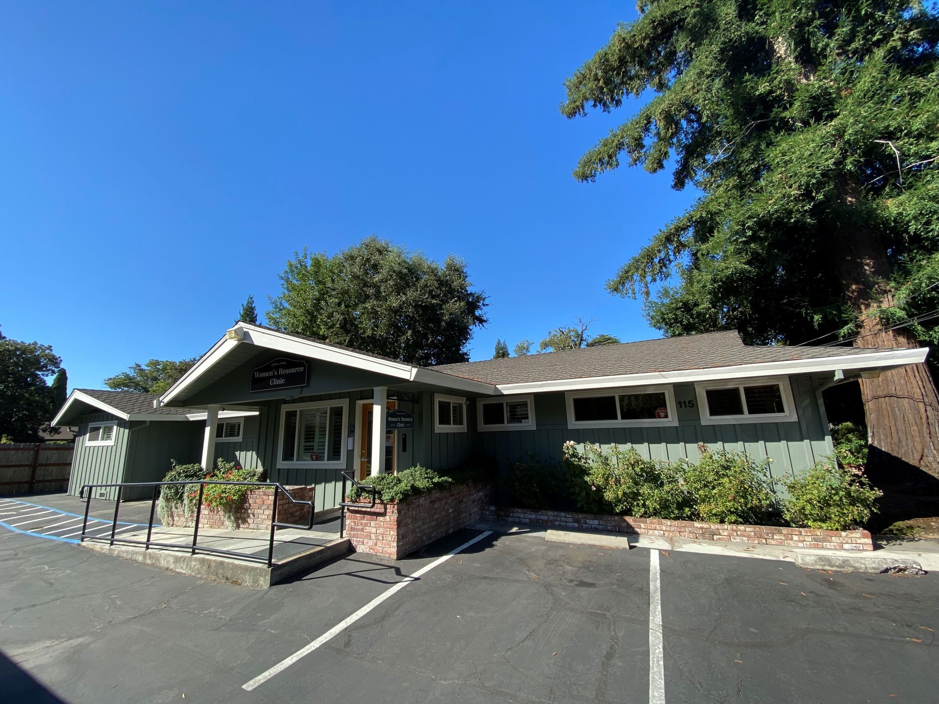 Green building with brick accents, wheelchair ramp, and parking spaces on a sunny day.