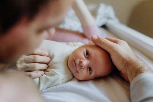 Father's hand gently touching a newborn baby's head while looking lovingly at the baby.