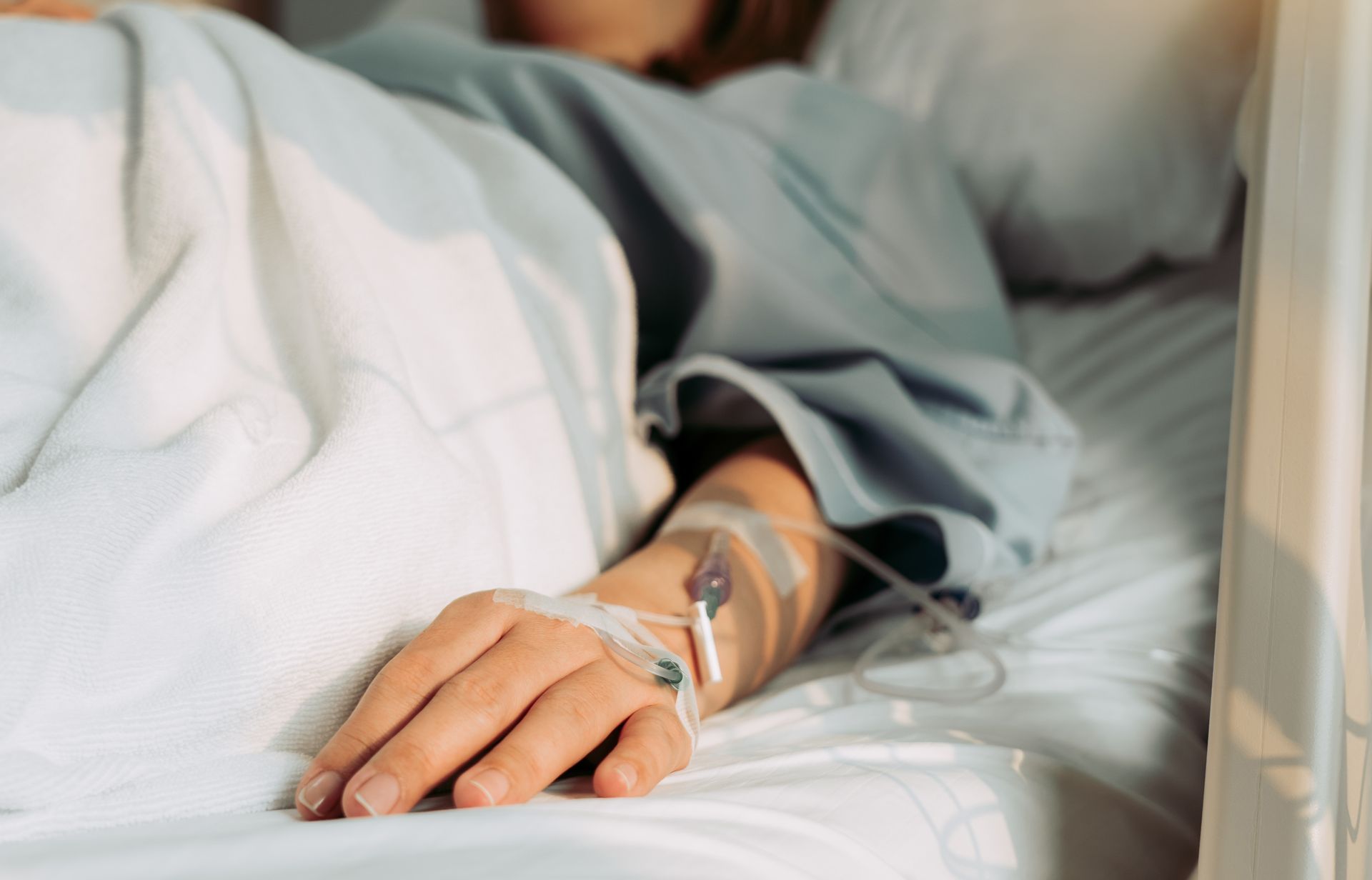 Person in a hospital bed with an IV in their arm, covered in a blanket.