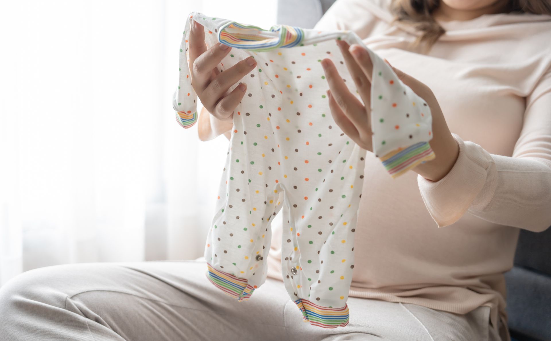 Woman holding a baby onesie with colorful dots, possibly preparing for a baby.