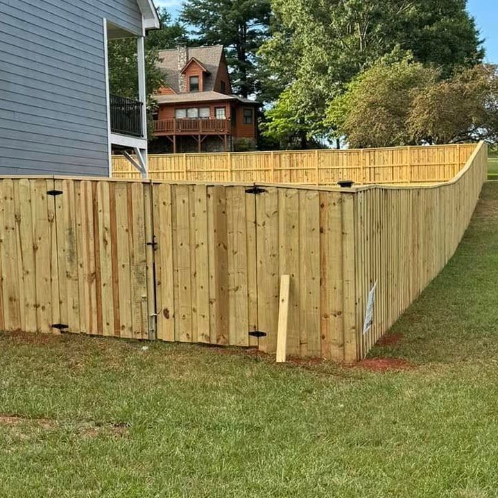 Wooden privacy fence surrounding a grassy backyard beside a house, with trees and a neighboring home in the background.