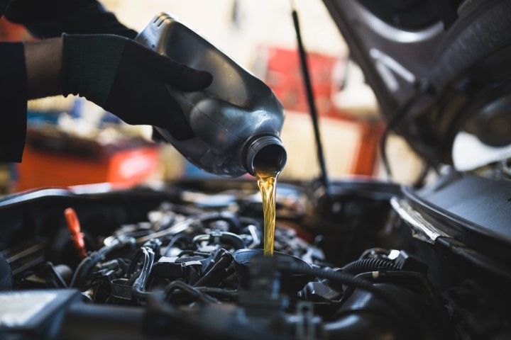 Oil pouring from a black container into an engine bay during an oil change
