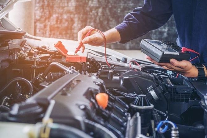Mechanic testing a car battery with jumper cables under the hood in a garage