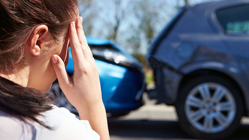 distressed woman looks at aftermath of a car accident