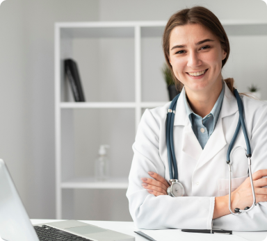 a female doctor is sitting at a desk with her arms crossed in front of a laptop computer .